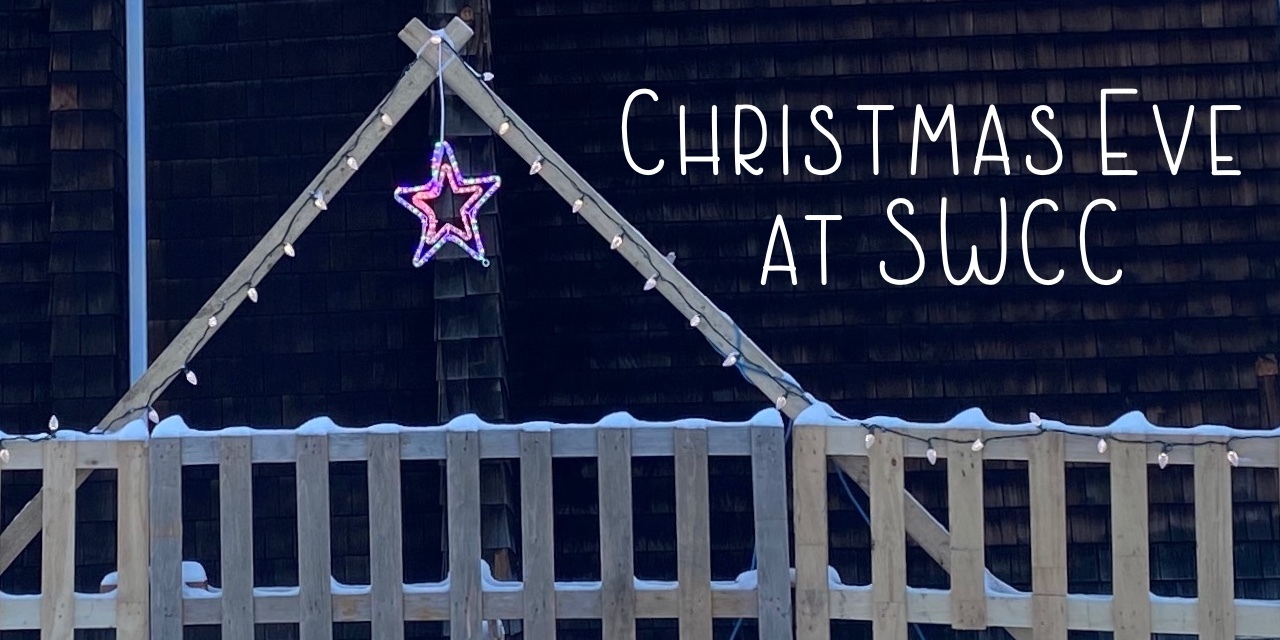 Rough wood made into a stable shape in front of a shingled church wall with a lit star hanging down