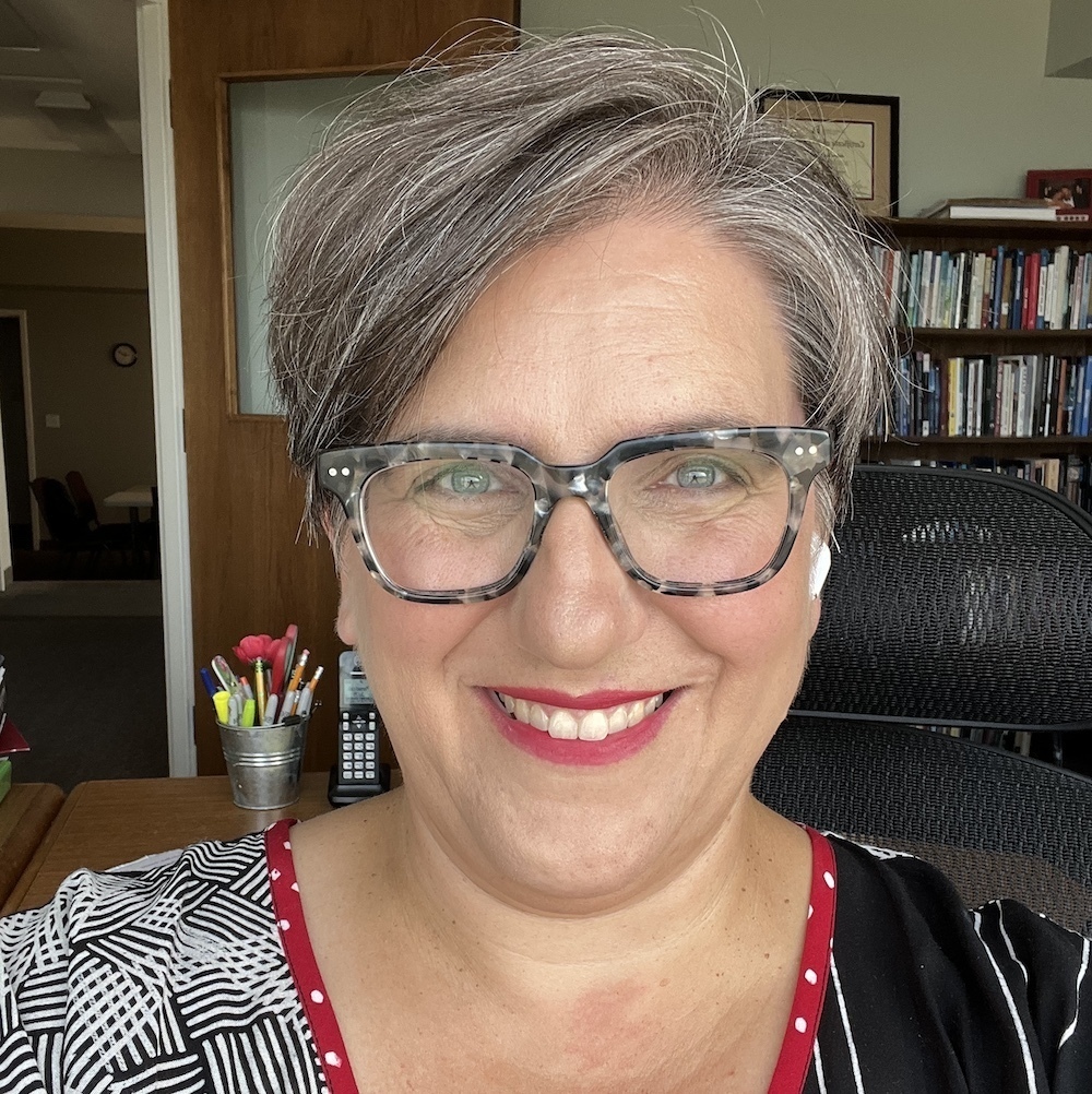 A photo of a smiling middle-aged woman with salt  pepper hair in front of a bookshelf